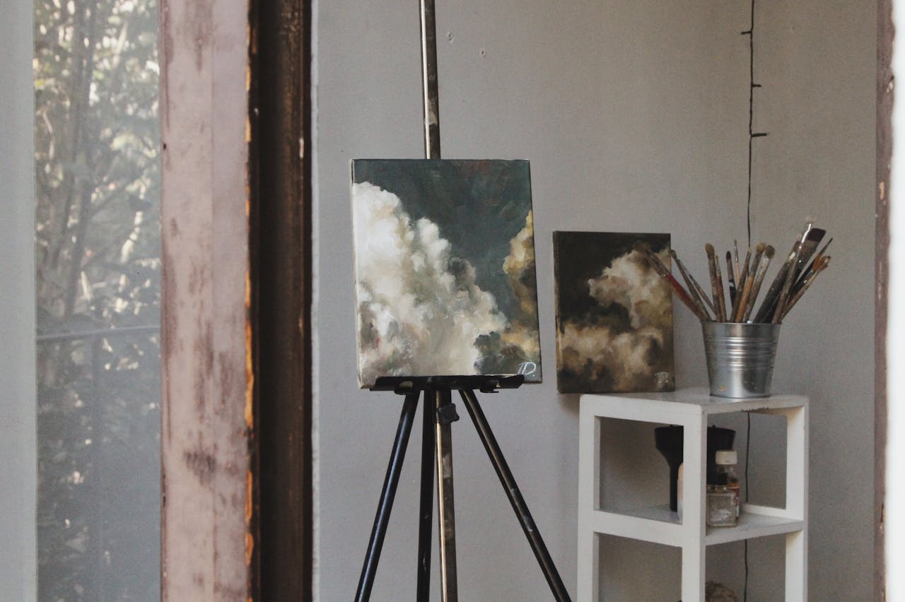 Cozy art studio featuring cloud paintings on easels and paintbrushes, captured indoors.